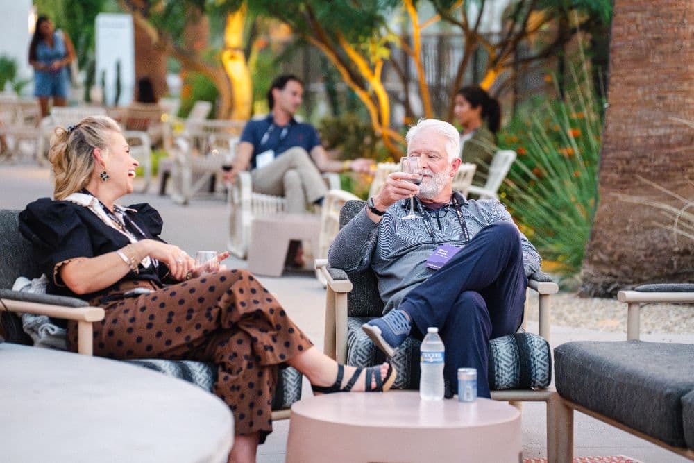 Two attendees laughing over wine on the patio at dusk