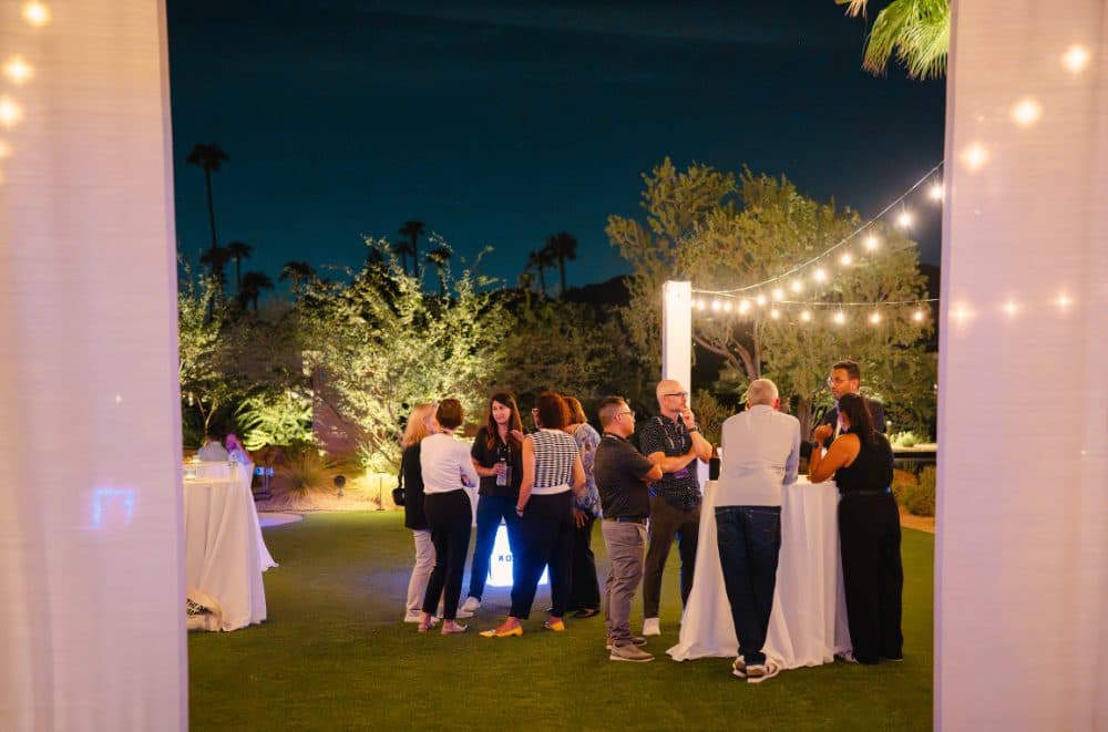 Attendees gathered around cocktail tables under string lights at night