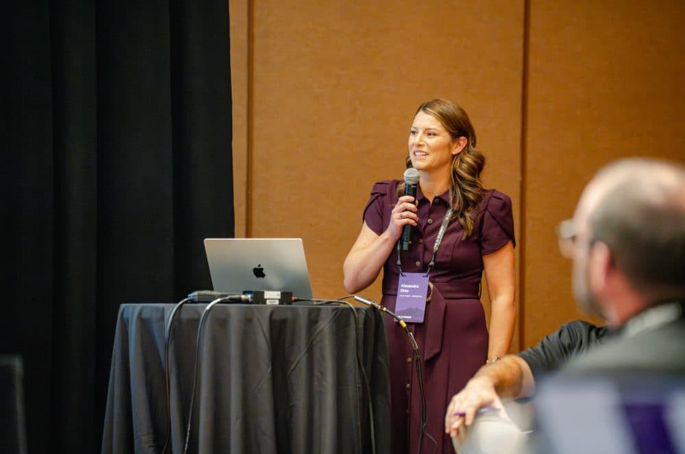 Speaker in a plum dress presenting at a table