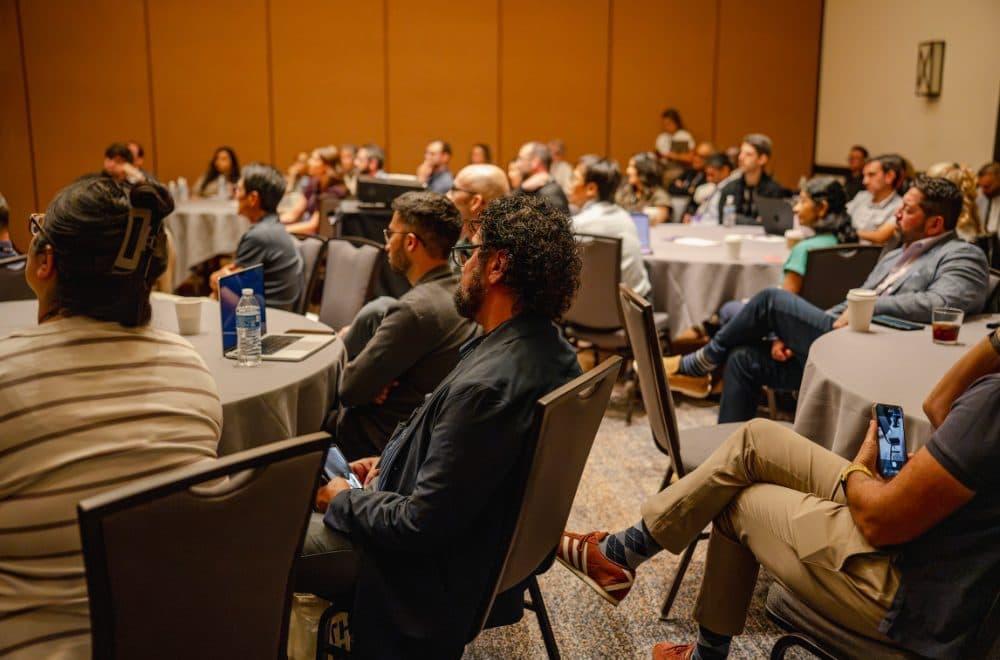 Attendees seated at round tables watching a talk