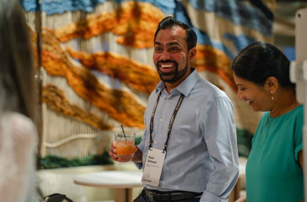 Attendee smiling with a cocktail in front of a woven desert mural